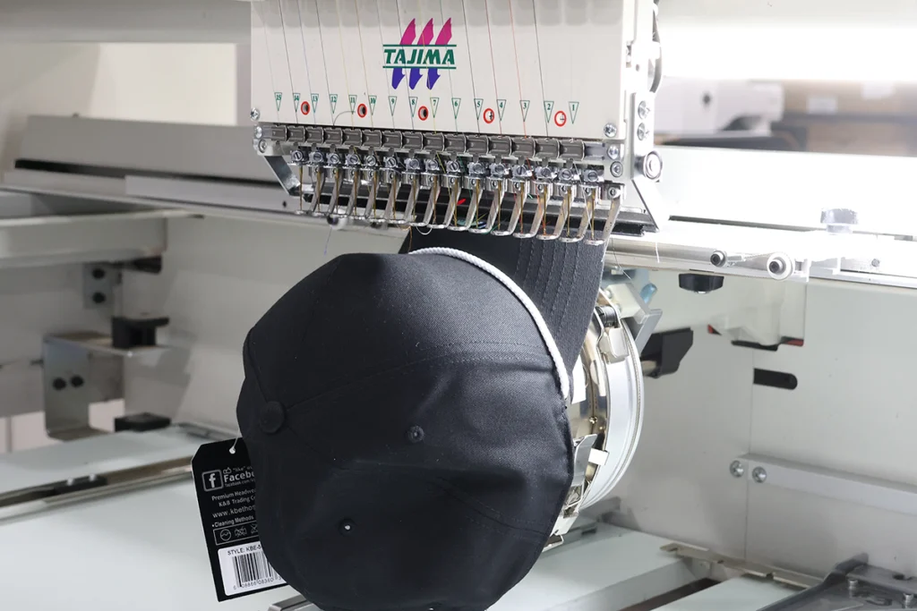 Black cap mounted on a commercial embroidery machine, ready to stitch